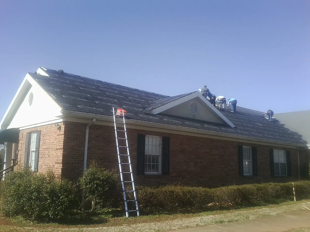 Crew tearing shingles off a brick ranch roof with a ladder set — Emergency Roof Repair work by our crew in El Dorado