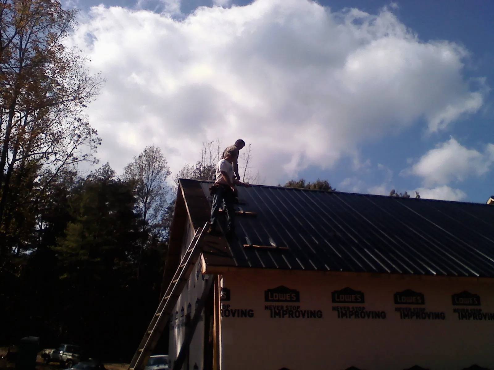 Roofer fastening dark metal panels high against a cloudy sky, from a Roof Inspection job in El Dorado