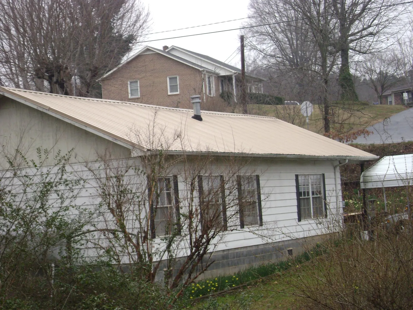 Tan metal roof on a white sided house set into a hillside — Commercial Roofing by Roofing Brothers in El Dorado